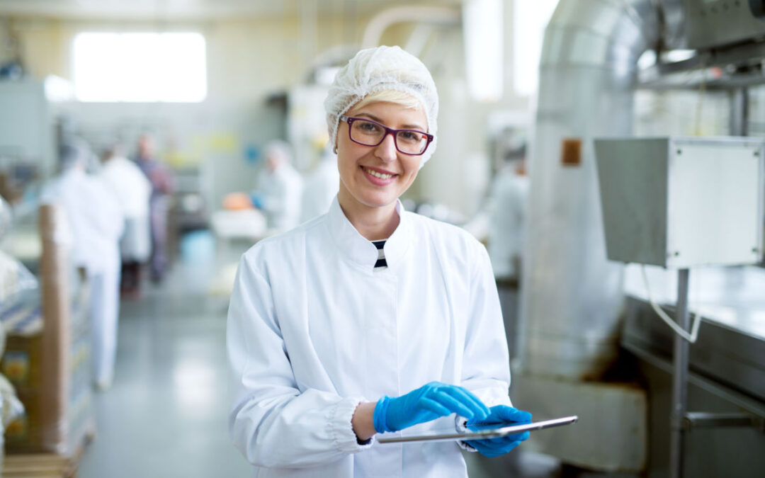 A woman in a lab coat smiling as she holds a tablet with blue gloves.