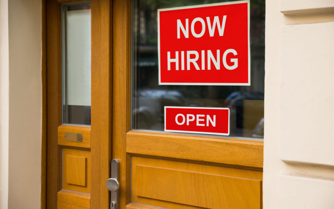 a "Now Hiring" sign on a wooden office door that also features an "Open" sign